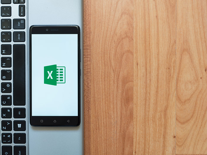 Microsoft excel logo image on a phone on top of a laptop