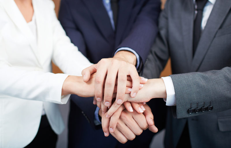 Business people put their hands one atop the other to form a team huddle.