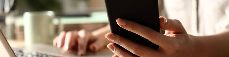 Cadrage sur les mains d’une personne qui utilise un téléphone intelligent et un ordinateur portable