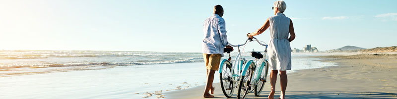 Deux personnes marchent sur une plage de sable en tenant un vélo.