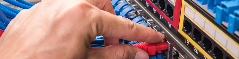 A close-up photograph of a IT professional plugging ethernet cable into a network server. 