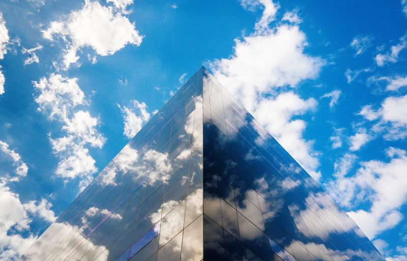 Cadrage sur un bâtiment dont les fenêtres réfléchissent le ciel bleu et les nuages.