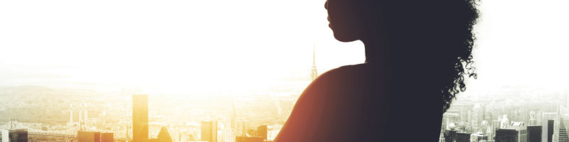 Silhouette of a businessperson looking out at a cityscape at sunrise.