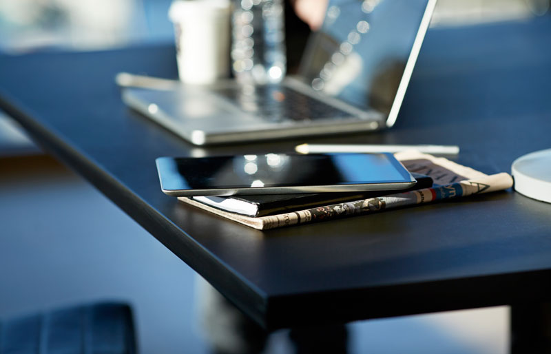 Cadrage sur un ordinateur portable, une tablette numérique et un calepin de notes posées sur un bureau de travail