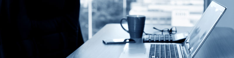 Cadrage sur un bureau où sont placés une tablette électronique, un ordinateur portable et une tasse de café